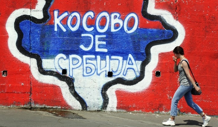 A woman walks past a map of Kosovo painted on a wall, with the words &ldquo;Kosovo is Serbia&rdquo;